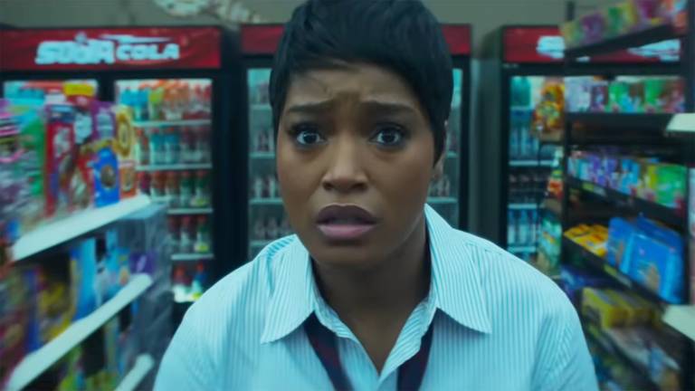 A Black woman standing inside a convenience store in a white collared shirt looks in the distance with a scared look on her face
